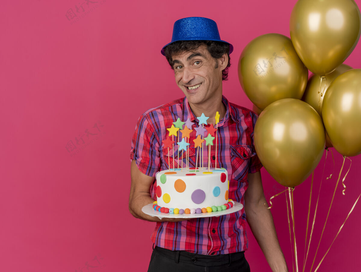 聚会微笑的中年白种人党男子戴着党的帽子拿着气球和生日蛋糕看着摄像机在深红的背景与复制空间隔离深红色复制男人