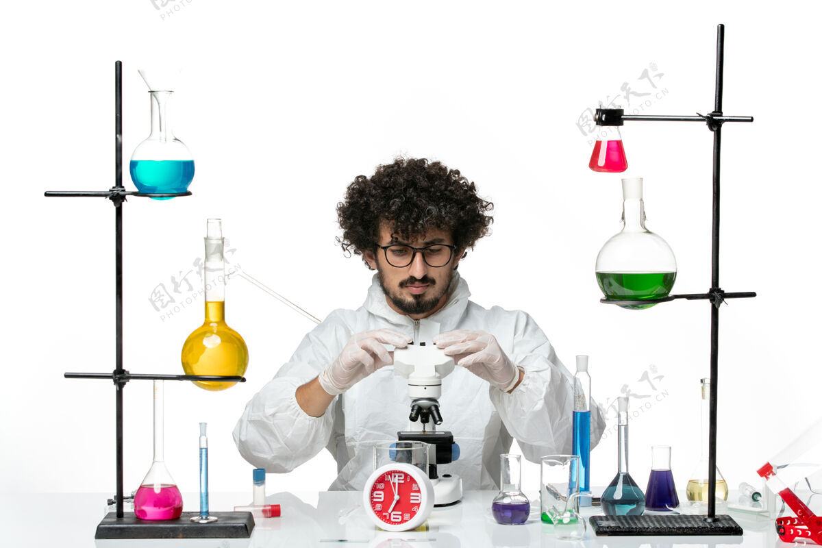 实验前视图穿着白色特别套装的年轻男科学家正在修理显微镜套装实验室瓶子