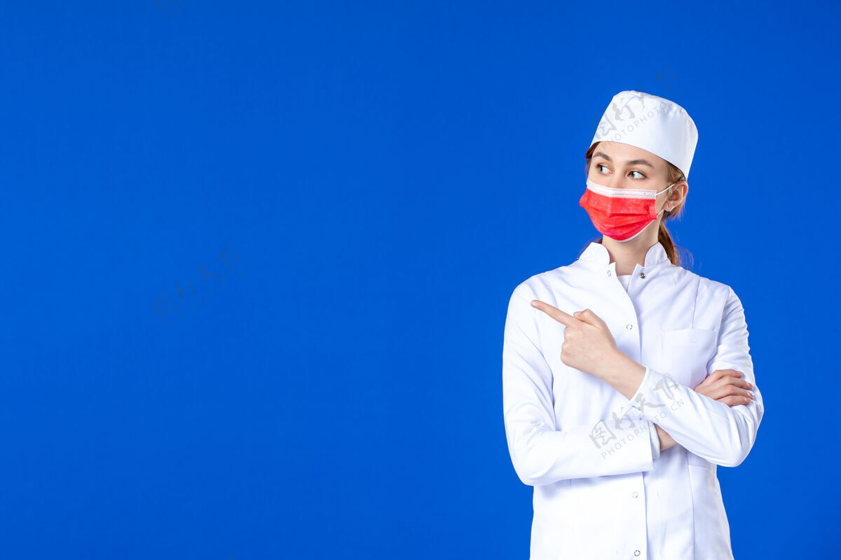 红正面图身着医疗服的年轻护士 蓝色墙上戴着红色防护面具蓝大流行医院