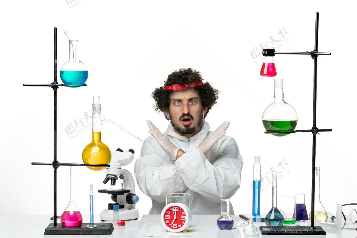 实验室正面图：年轻的男科学家穿着特殊的西装 戴着防护头盔 坐在科学实验室的白色办公桌上特殊化学防护