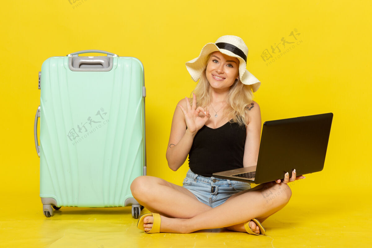 视野前视图年轻女性使用笔记本电脑在黄墙上航行度假女性旅行旅行太阳漂亮成人微笑