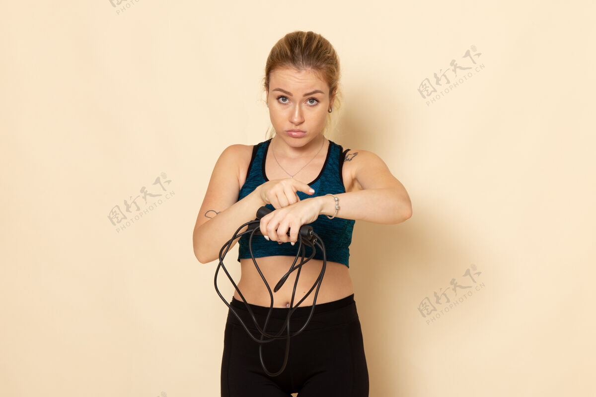身体正面图身着运动装的年轻女性手持跳绳在浅白的墙上健康锻炼身体运动美容操运动光肖像