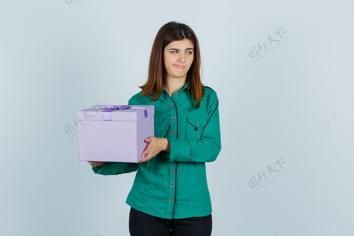恼怒年轻女孩拿着礼品盒 穿着绿色上衣 黑色裤子 看起来很不高兴前视图愤怒抱着女人