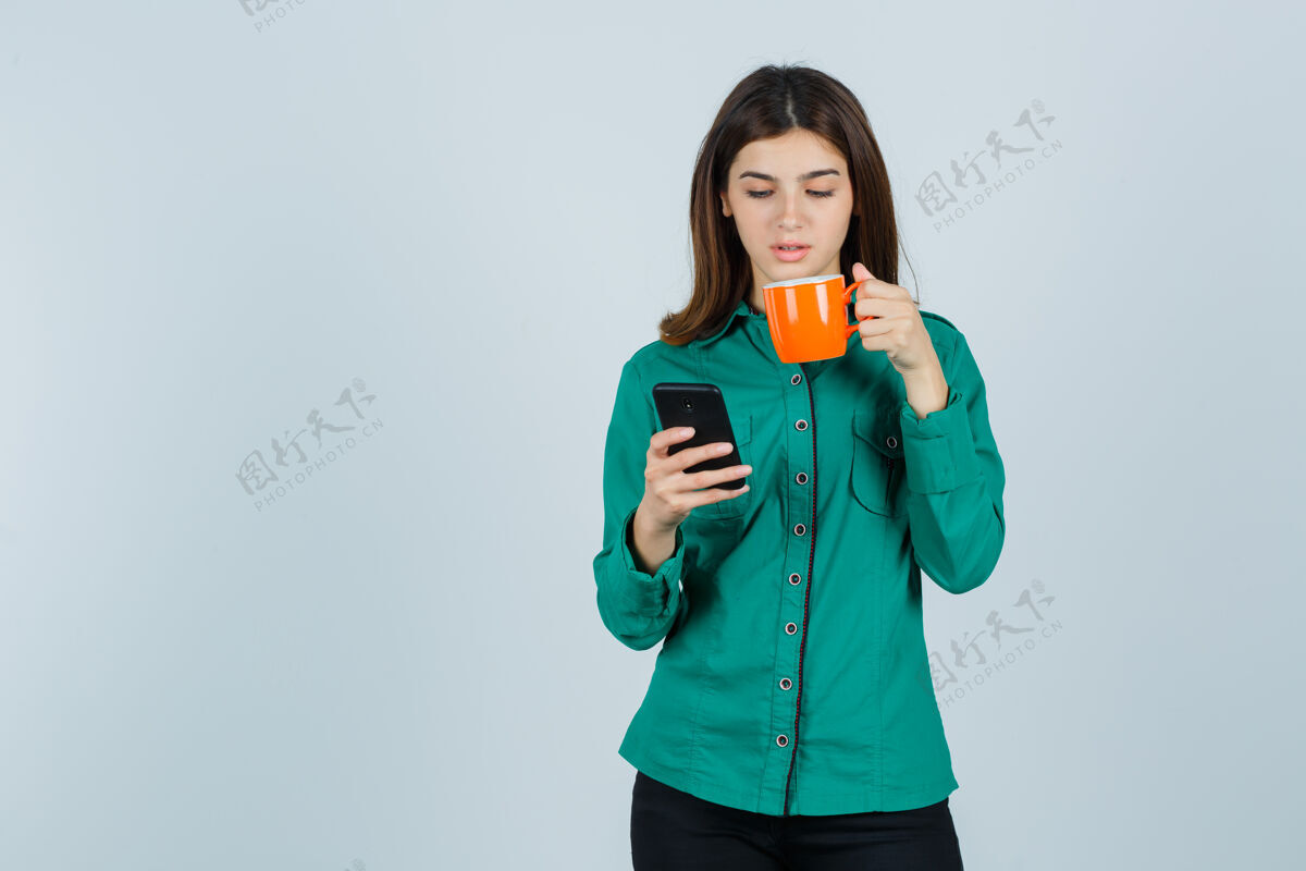 头发穿着衬衫的年轻女士手里拿着桔黄色的茶杯和手机 看上去自信满满 前视尽收眼底年轻茶护理