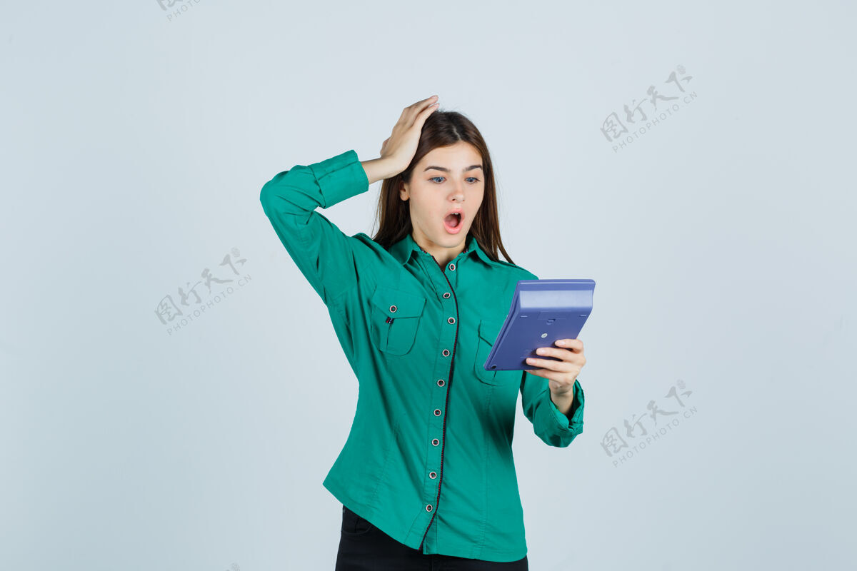 前面年轻女士看着计算器 手放在头上 穿着绿色衬衫 看起来很震惊 前视图女性女人漂亮