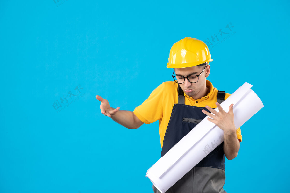 蓝色身穿黄色制服和头盔的男性建筑工人正视图 蓝色墙上有平面图人计划前面