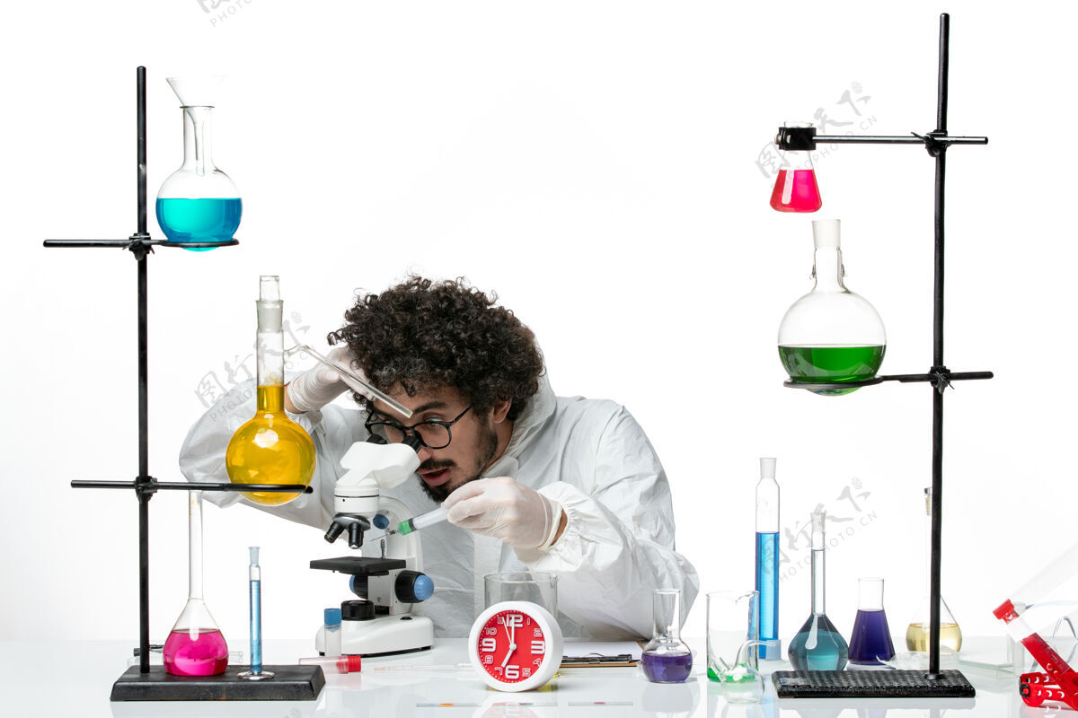 实验室前视图穿着特殊套装的年轻男科学家在白墙上使用显微镜生物特殊视图