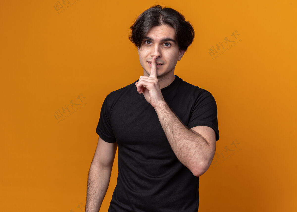 沉默穿着黑色t恤的年轻帅哥在橘色的墙上表现出沉默的姿态男人手势年轻