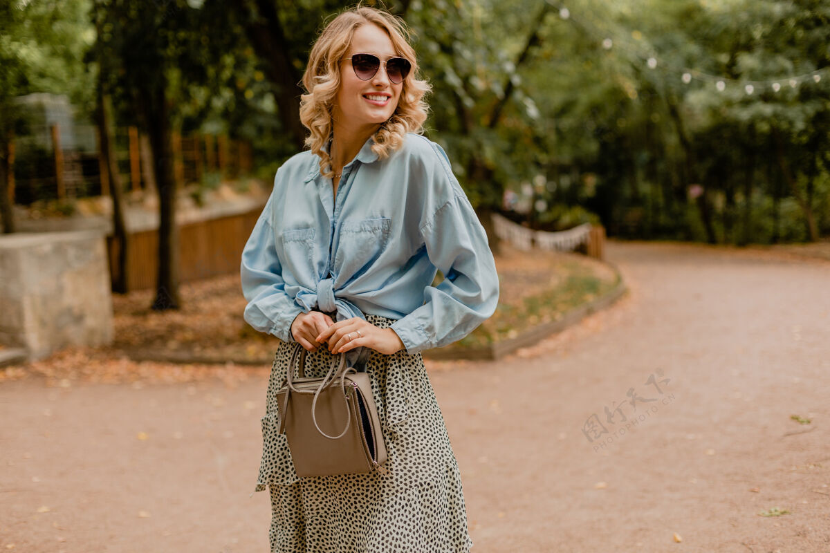 手提包迷人的金发微笑的女人穿着夏天的行头走在公园里表情衣服装束