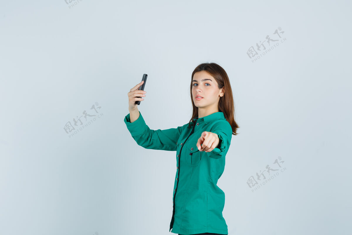 手机一张年轻女士在手机上自拍的照片 她穿着绿色衬衫 指着相机 看起来很自信华丽专业人物