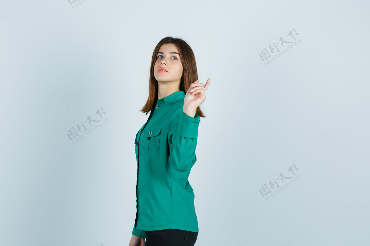 站立年轻的女性摆姿势 指着后面的绿色衬衫 看起来很自信工作女士欢呼