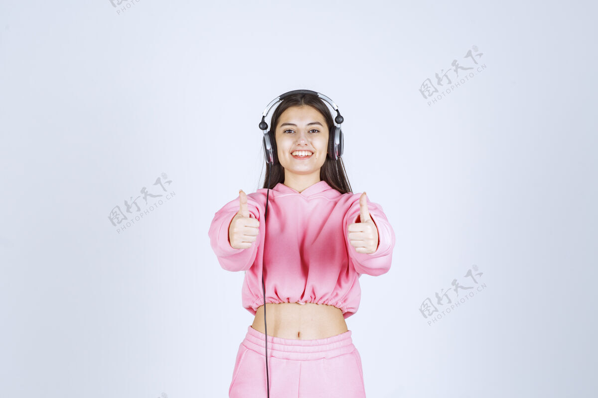 喜欢穿着粉色睡衣的女孩戴着耳机 展示着享受的标志高质量的照片休闲播放列表Ok