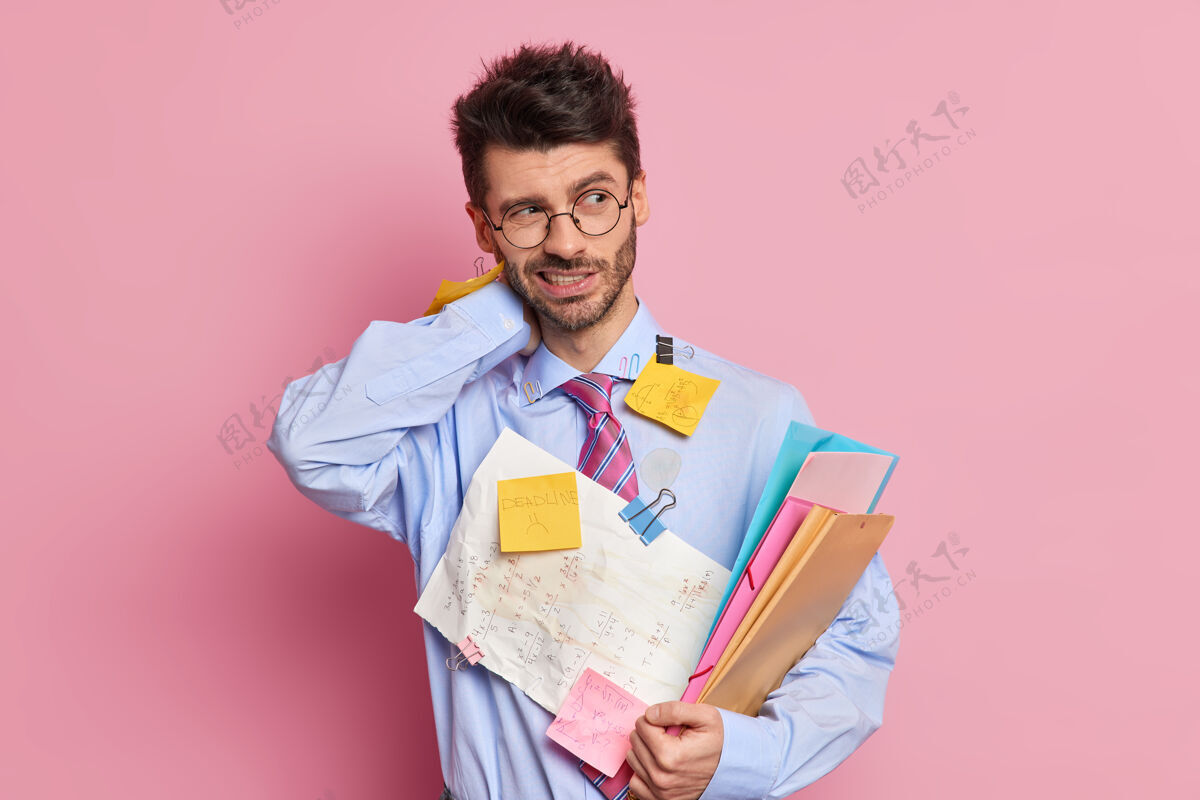 企业家疲惫不堪的员工脖子痛 拿着文件夹 穿着附有便签的衬衫 写着信息贴纸男性项目