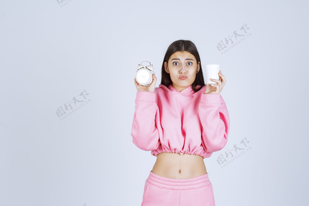 女人穿着粉色睡衣的女孩 手里拿着闹钟和咖啡 一脸疲惫常规人类拍照
