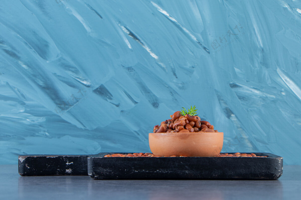自制豆子碗在豆子板上 在蓝色的背景上生的美味的餐盘