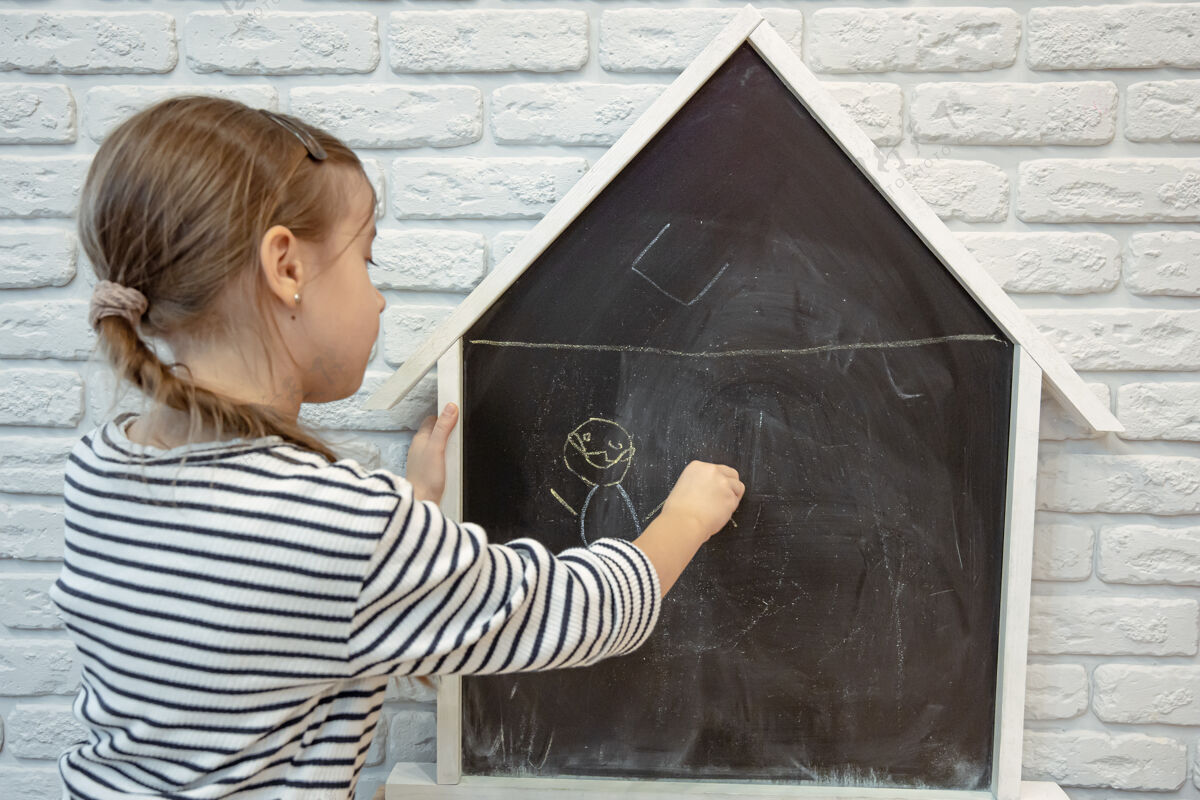 背一个小女孩用粉笔在黑板上画房子的形状粉笔学习黑板