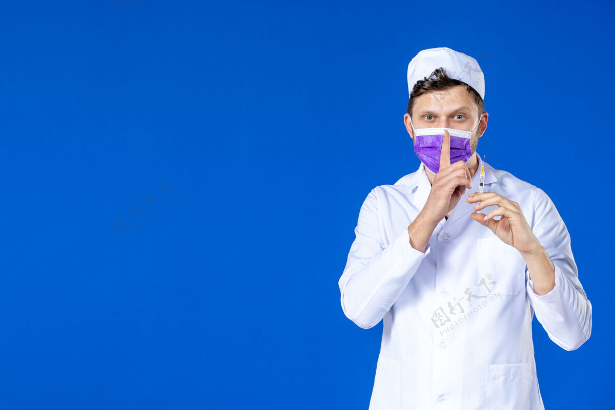 注射前视图中的男医生穿着医疗服和口罩持有疫苗和注射在蓝色男医生病毒药品