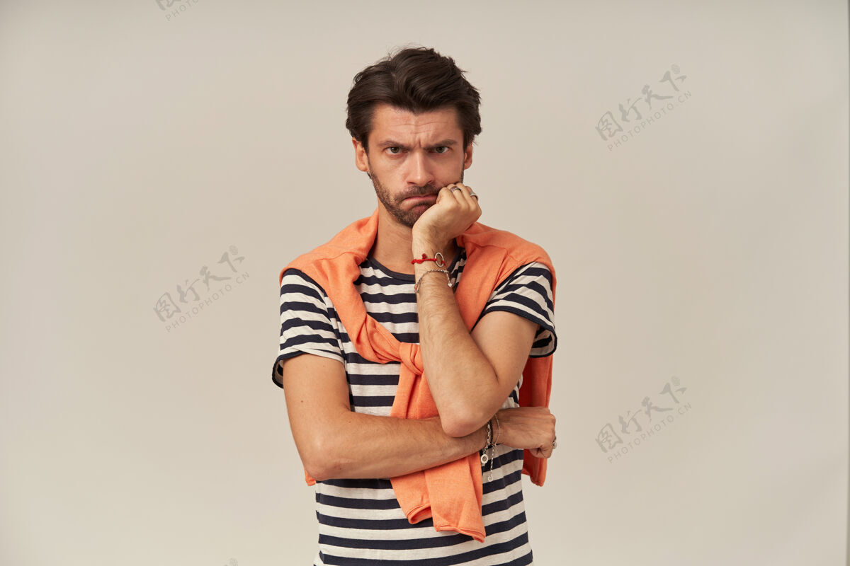 专注一个黑发硬毛的心烦意乱的男人穿着条纹t恤 肩膀上绑着橘色毛衣把下巴靠在手上30秒下巴外表