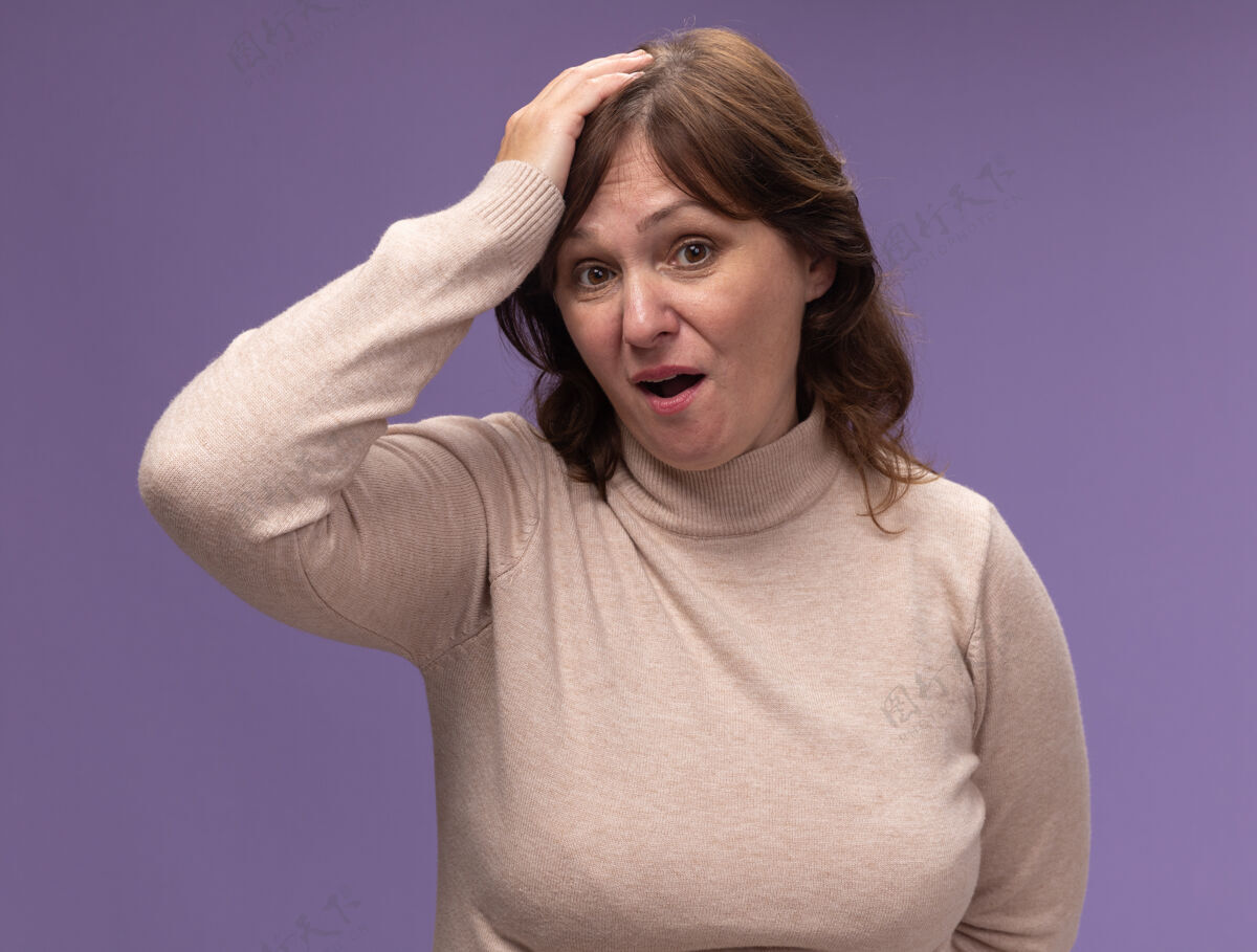 错误穿米色高领套头衫的中年妇女迷茫了 手放在头上 非常焦虑 因为她站在紫色的墙上时出错了困惑高领毛衣年龄