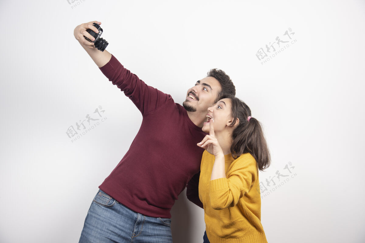 家庭一对可爱的情侣拿着相机自拍 在白墙上摆姿势微笑摄影师朋友