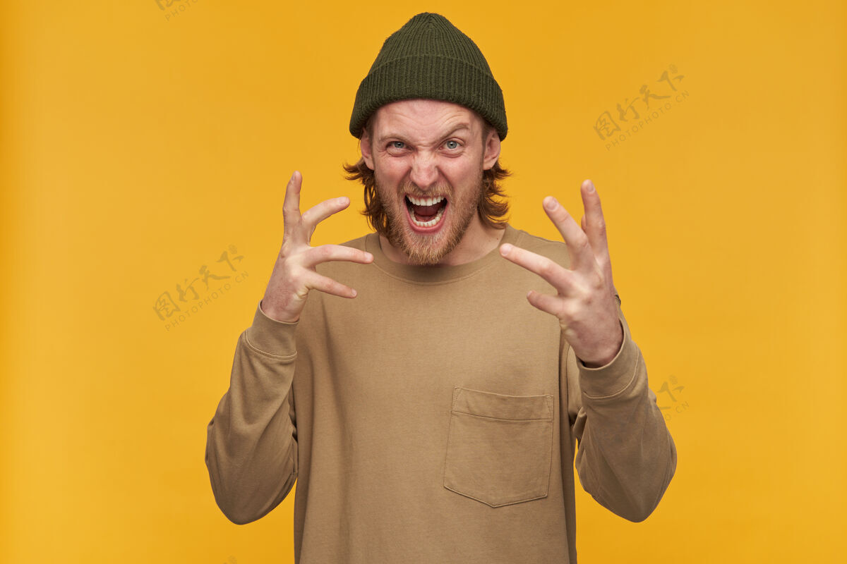 肖像一个满脸怒容 满脸胡须 金发的男人 穿着绿色小珠子和米色毛衣 做着可怕的鬼脸隔着黄墙隔离阳刚肤色年轻