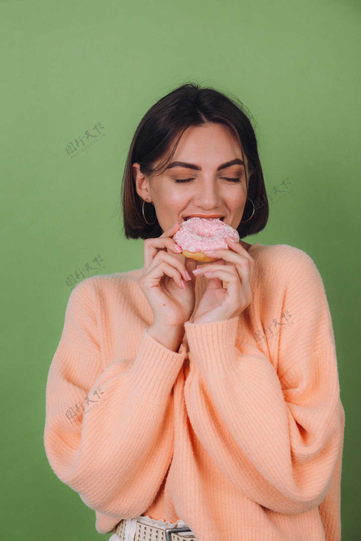 年轻穿着休闲桃色毛衣的年轻时尚女性 隔离在绿色橄榄色墙壁上 粉色甜甜圈快乐复制空间女人搞笑饥饿