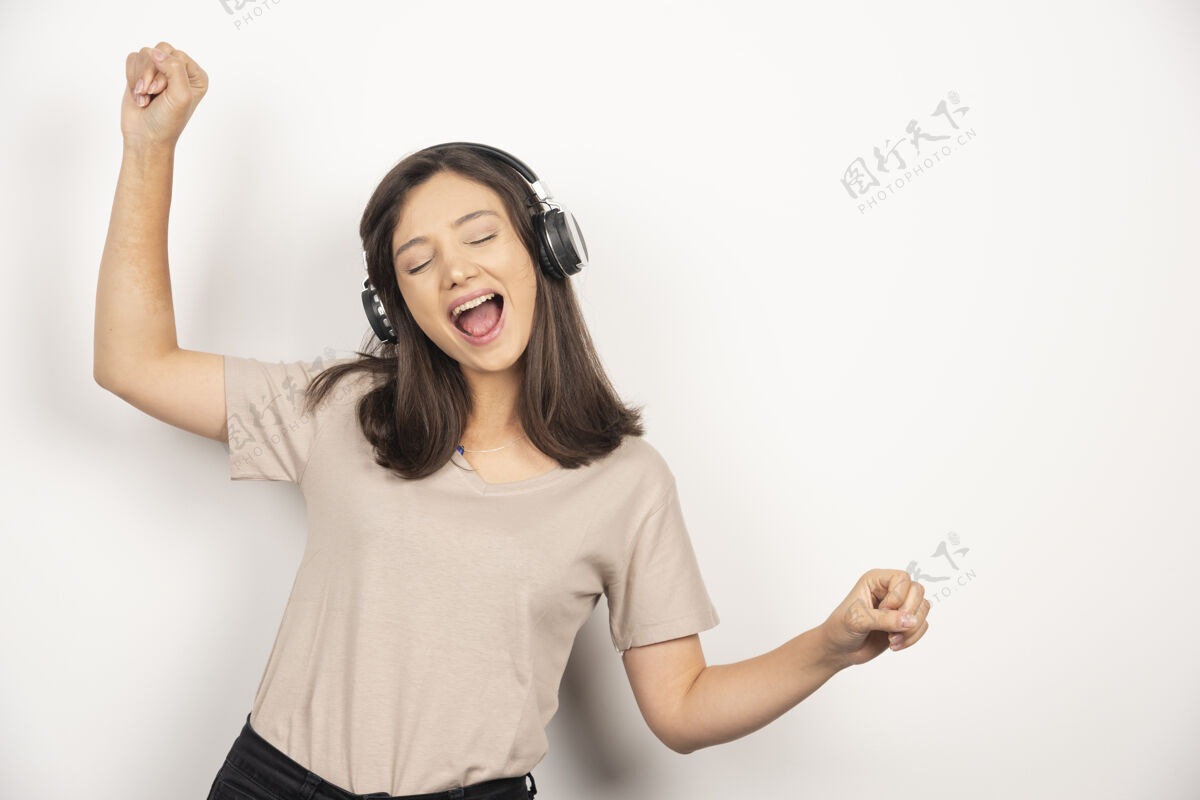 耳机穿着米色衬衫的快乐的年轻女子一边跳舞一边戴着耳机听音乐享受人乐趣
