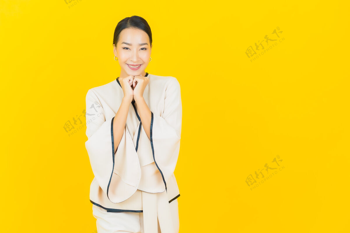 模特美丽的亚洲年轻商业女性在黄色墙上穿着白色西装微笑的画像时尚可爱女士