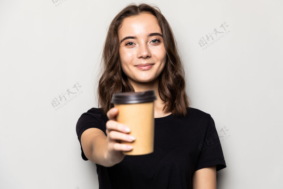 持有年轻漂亮的女人提供白色咖啡杯隔离在灰色的墙上年轻茶卡布奇诺