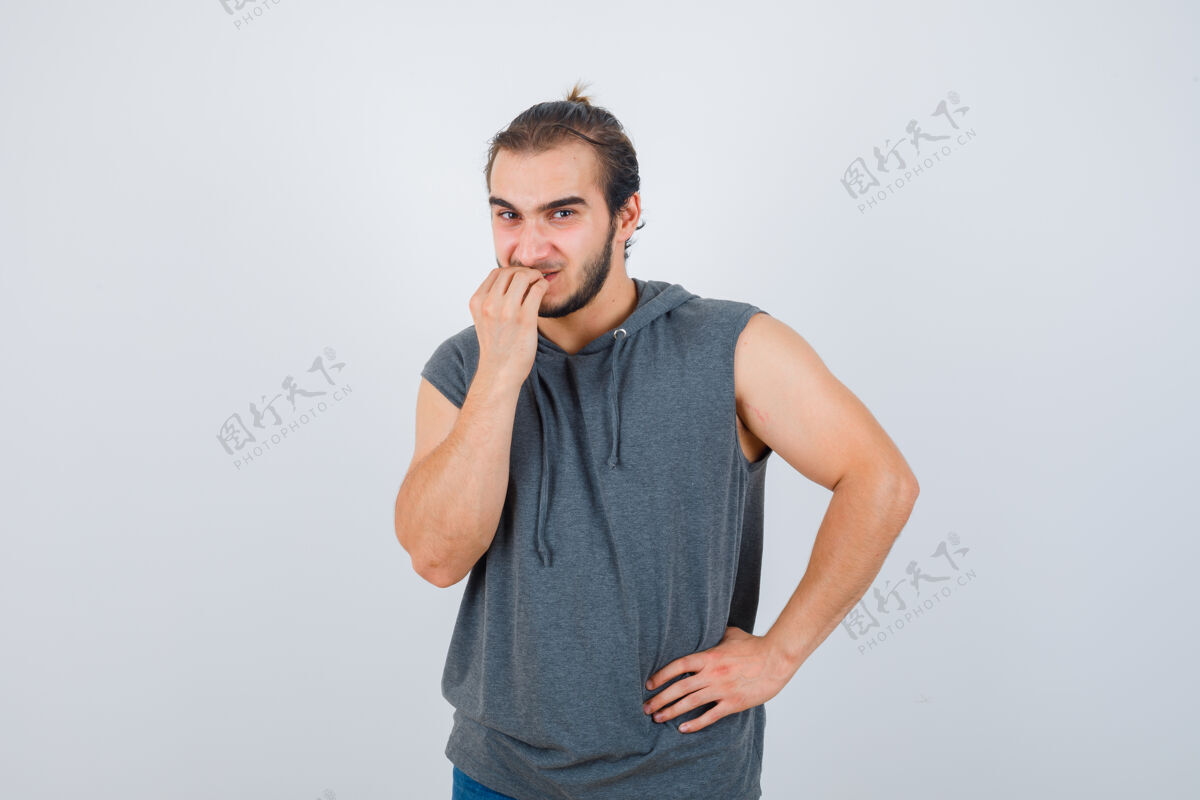 沮丧年轻健康的男性在无袖连帽衫咬指甲的肖像 看起来有压力的前视图正面工人年轻