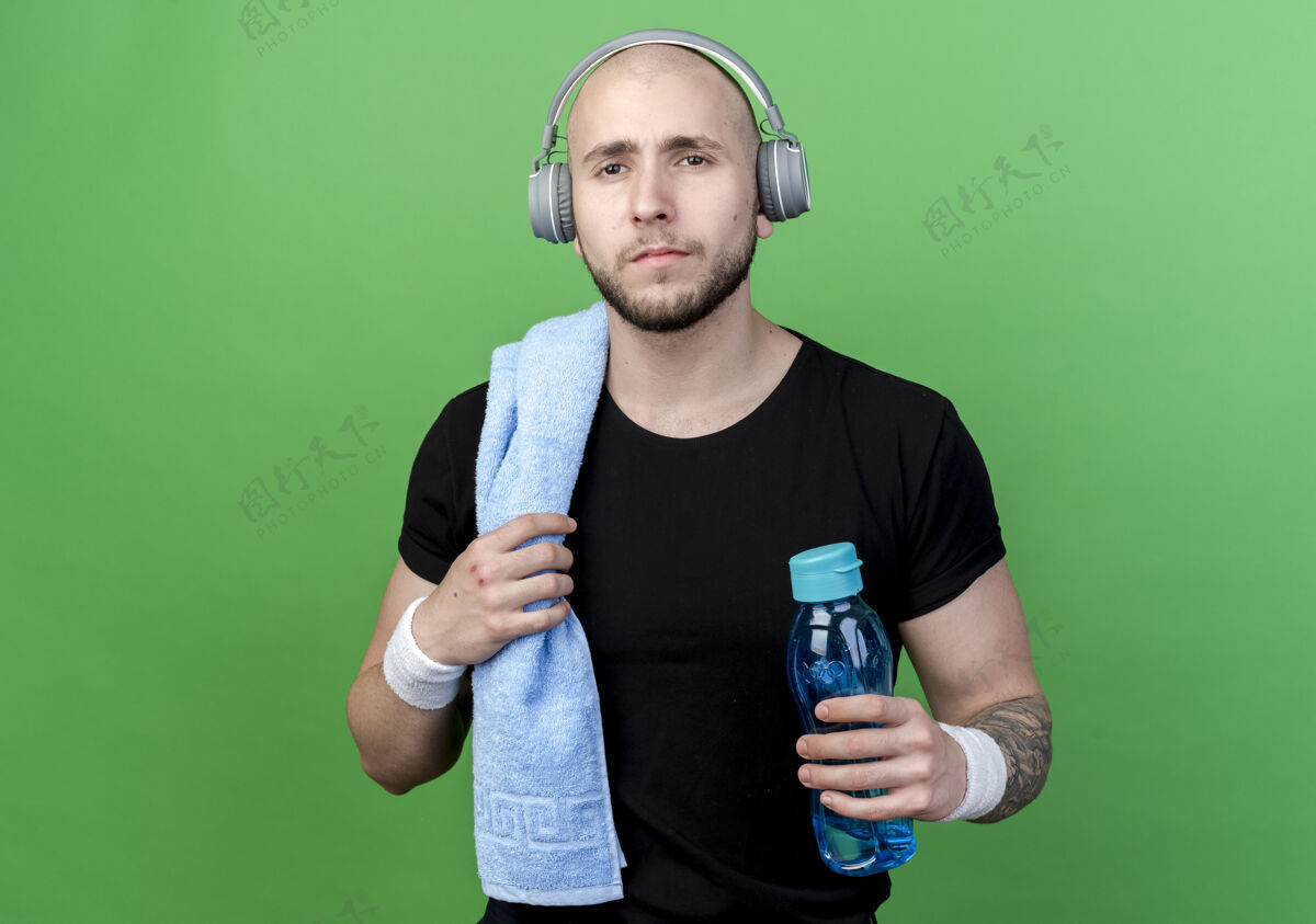 耳机年轻的运动型男子戴着腕带和耳机 肩上扛着毛巾的水瓶瓶子腕带毛巾