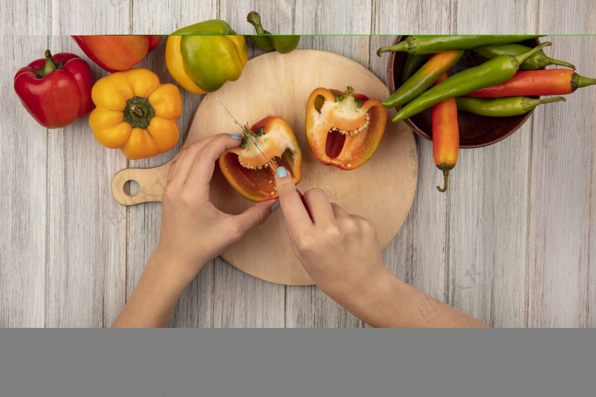 蔬菜顶视图女性手切割橙色甜椒在木制厨房板上用刀在灰色木制表面配料食物女性