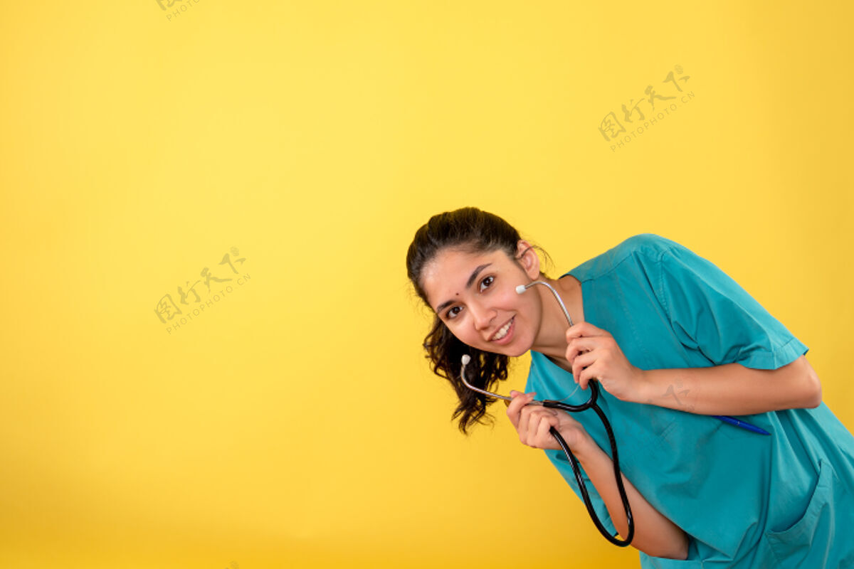 背景正面图微笑的年轻女医生手持听诊器在黄色背景上听诊器微笑肖像