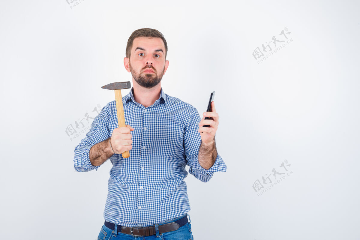 男人年轻的男性拿着手机 把锤子放在衬衫 牛仔裤里 表情严肃正面图保持休闲肖像
