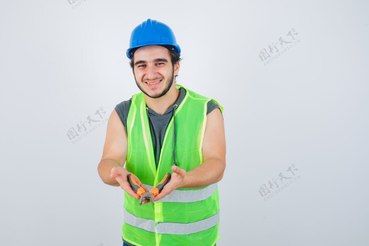 钳子年轻的建筑工人穿着工装展示钳子 看上去很高兴 正面图工作服欢呼英俊