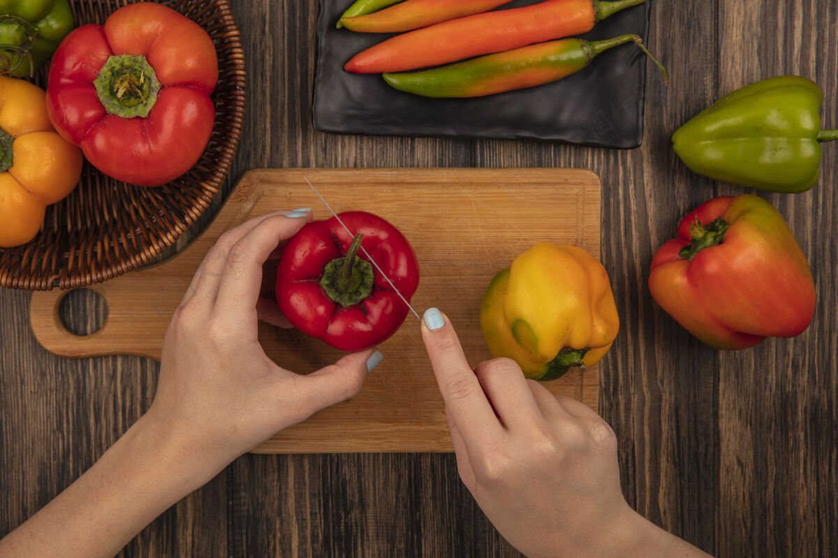 食物俯视图中的女性手切割新鲜芳香的甜椒在木制厨房板上用刀在木制表面蔬菜切割刀