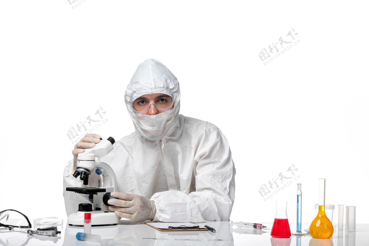 大流行前视图男医生穿着防护服 戴着面罩 在空白处使用显微镜正面防护套装