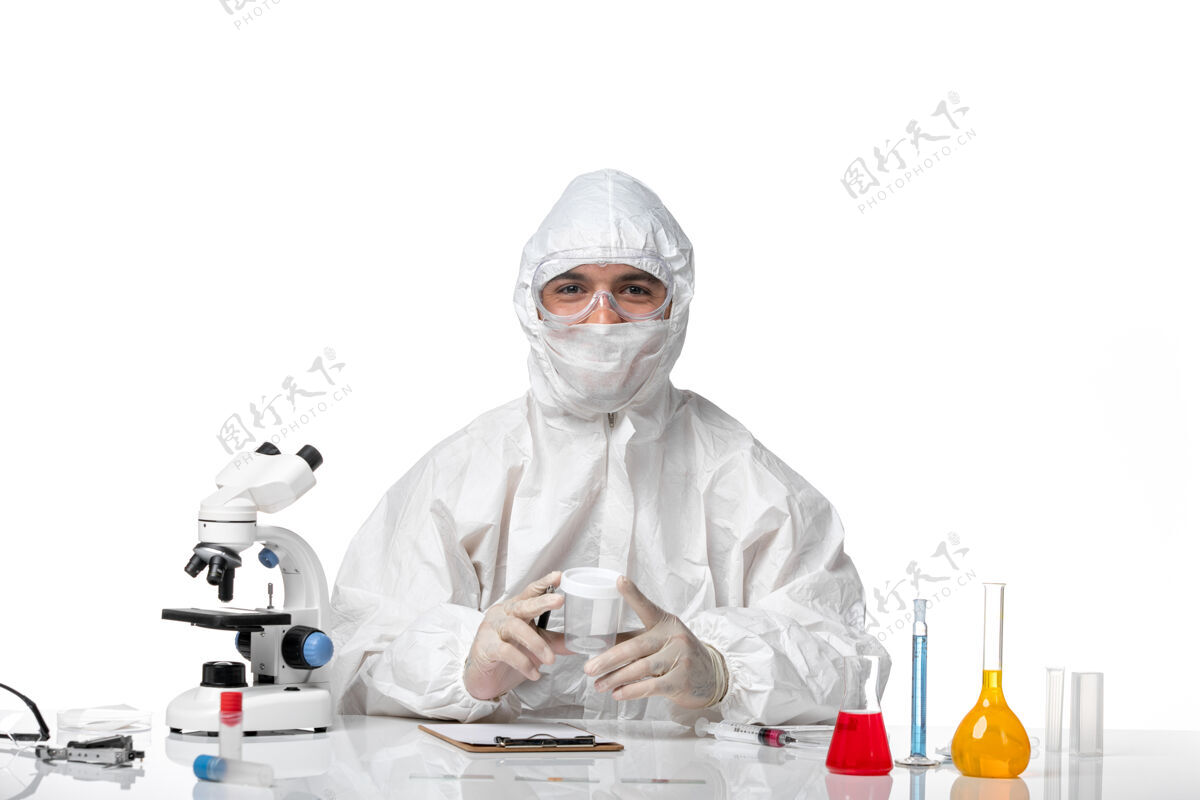 持有正面图穿着防护服的男医生拿着空瓶子 在白桌子上写字药品正面西装