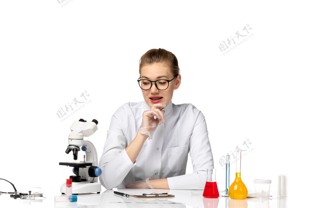 手套前视图穿着医疗服戴着手套的女医生坐在白色的桌子上 拿着解决方案医疗工作专业人员