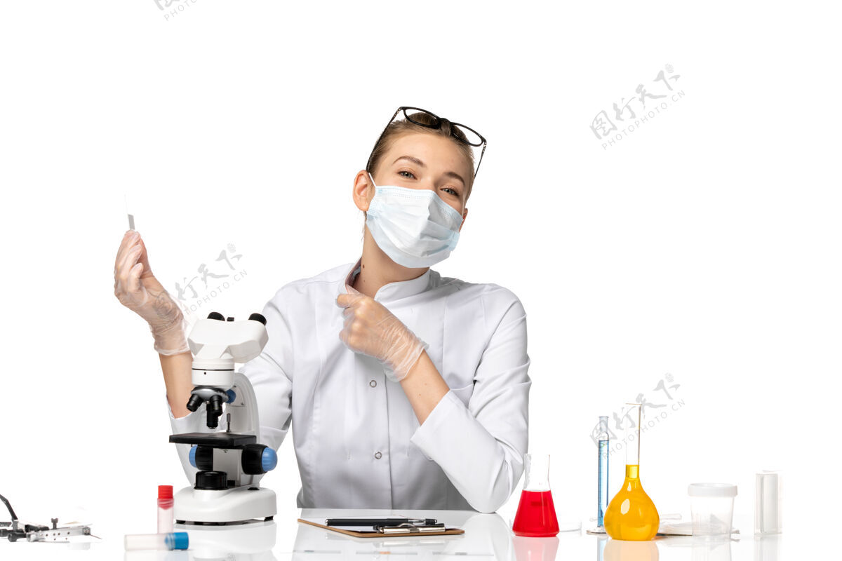 病毒前视图穿着医疗服的女医生戴着面罩 因为科维德在白色办公桌上用溶液工作前台面罩办公桌