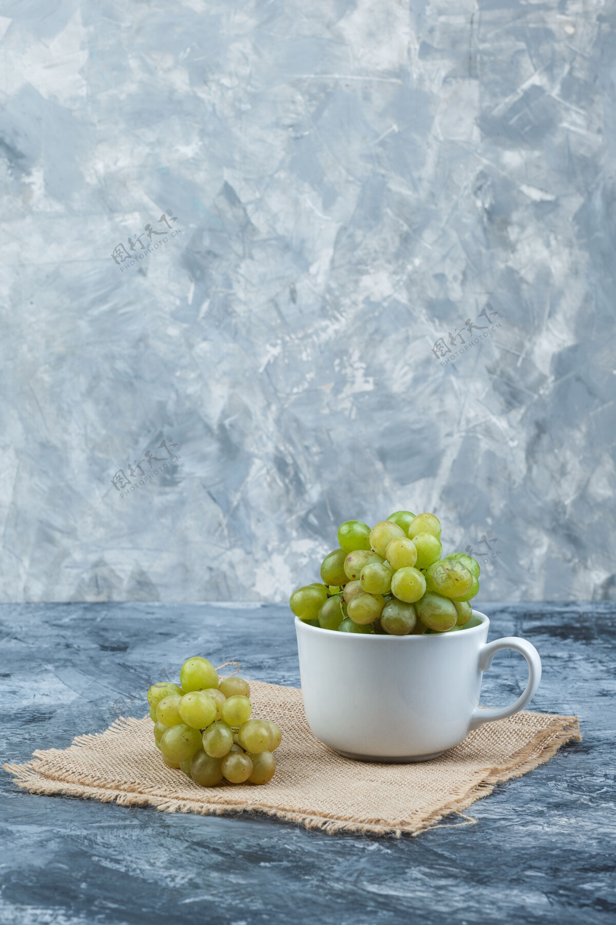 浆果绿色葡萄在一个白色的杯子侧视图上的垃圾和一块麻袋背景树枝果汁酒厂