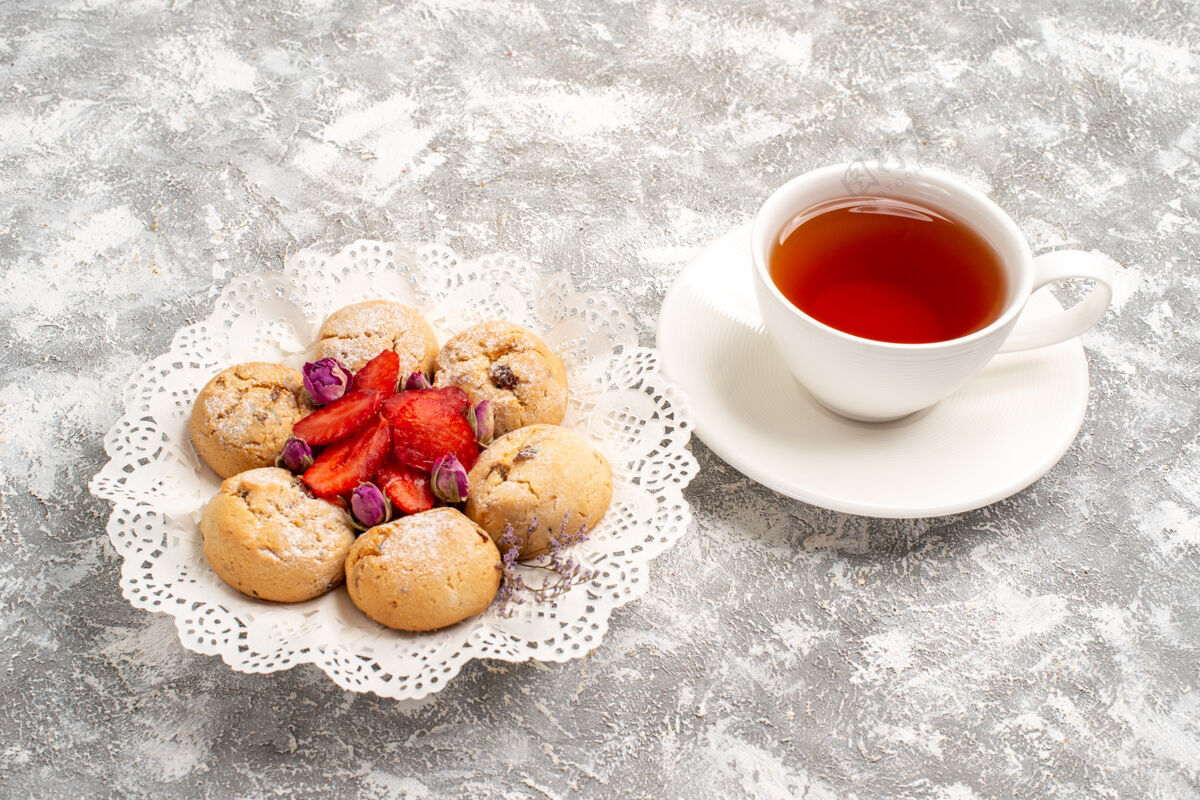 水果正面是美味的沙曲奇和新鲜的草莓和一杯茶在白色空间茶碟饼干新鲜的