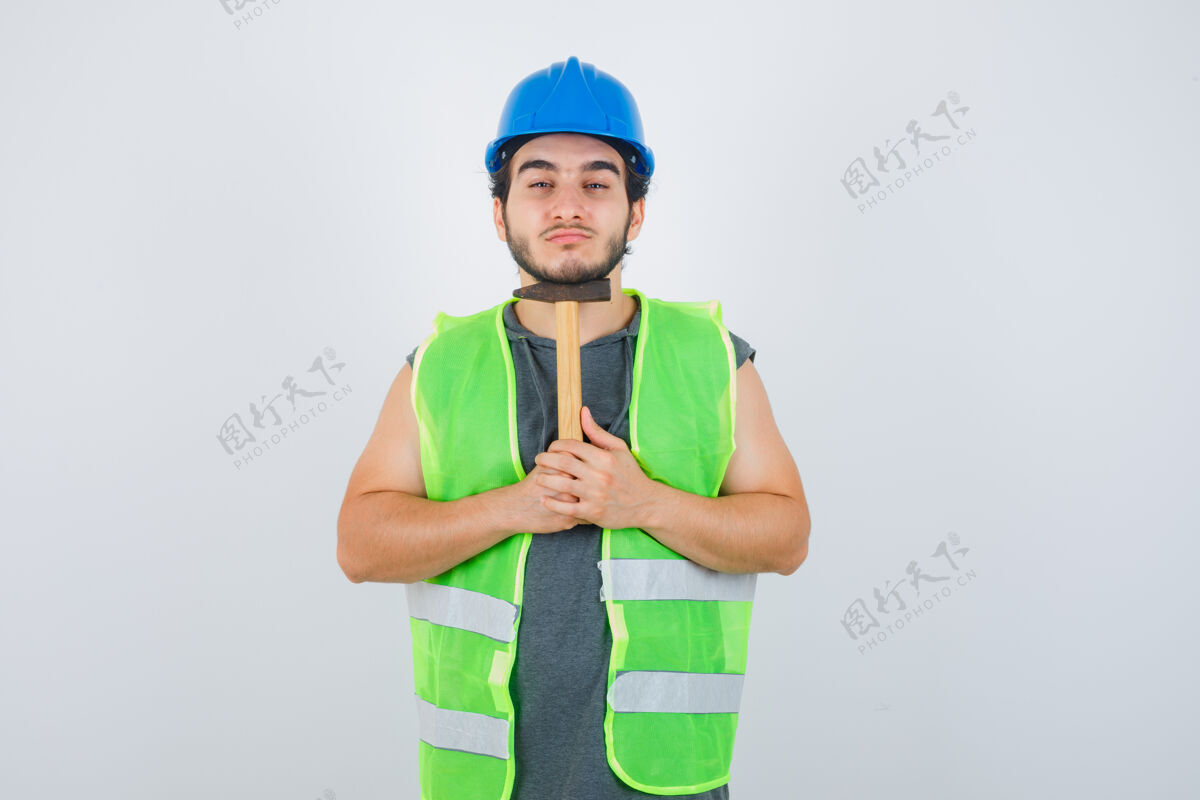男性年轻的建筑工人穿着工作服 下巴下拿着锤子 看上去很自信 正对着前方成人严肃时尚
