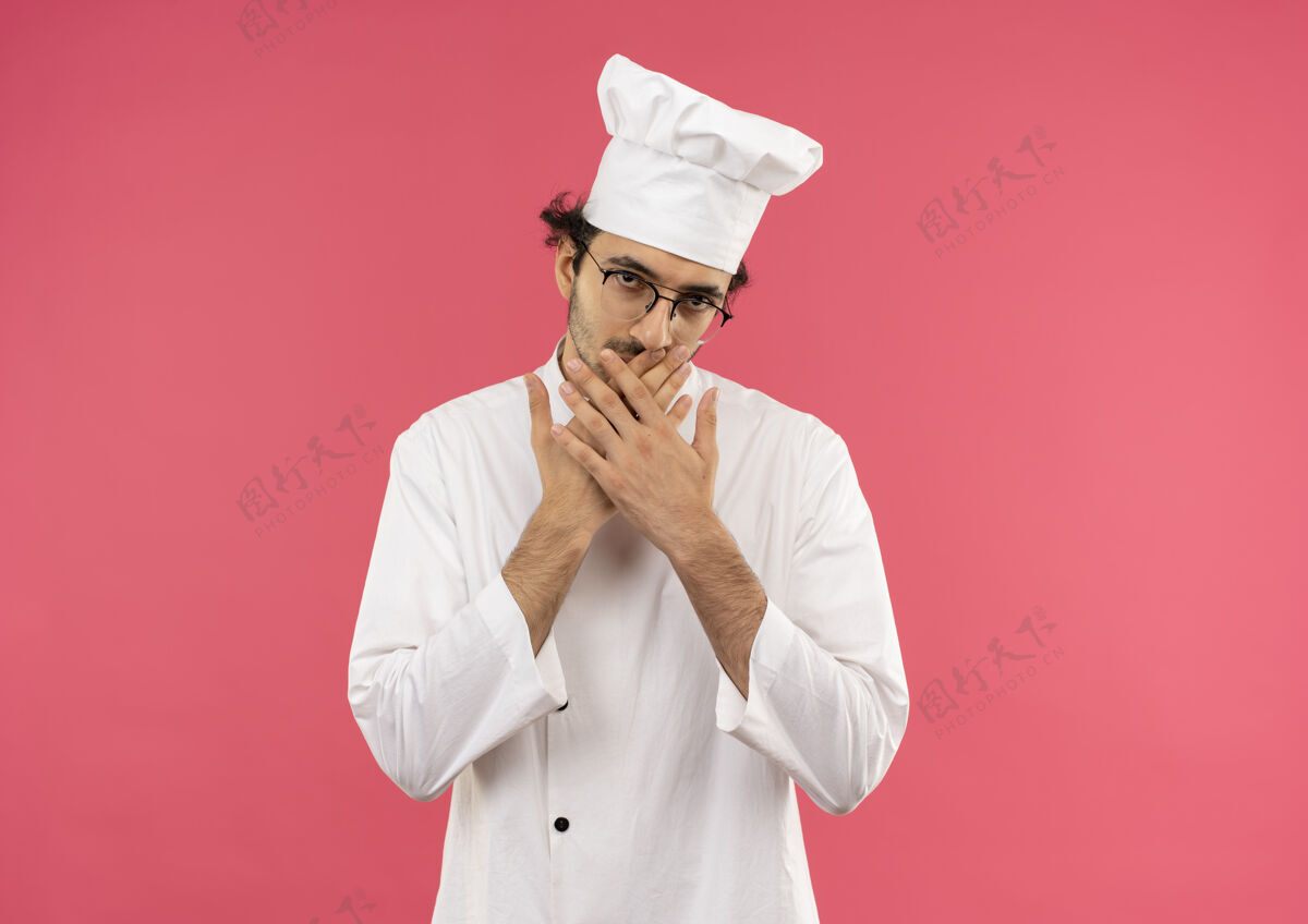 男年轻的男厨师穿着厨师制服 戴着眼镜 双手捂着嘴粉红穿烹饪