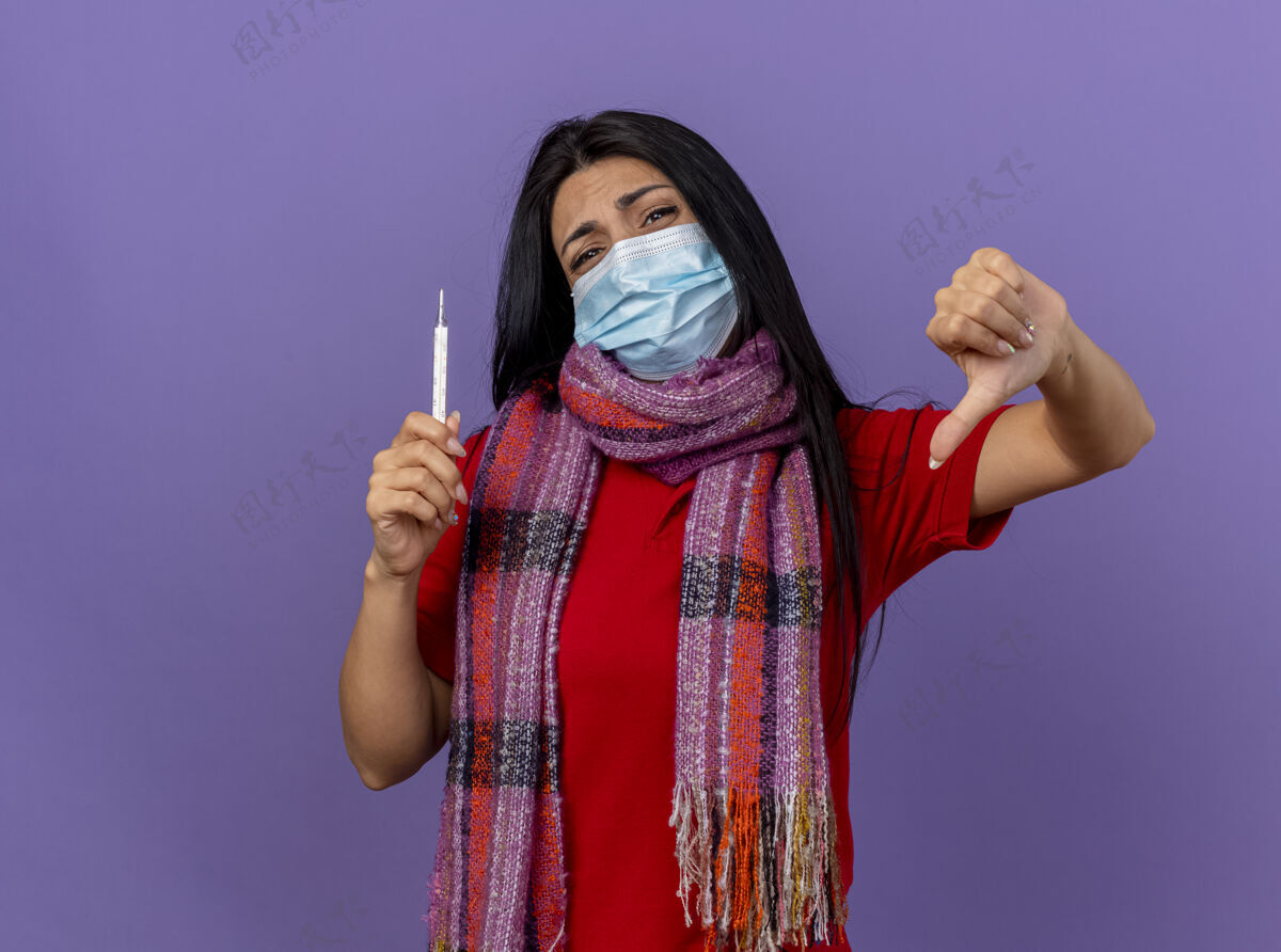 围巾戴着面具 戴着围巾 拿着温度计 拇指朝下的年轻白种人生病的女孩被隔离在紫色的墙上 留着复印空间体温计年轻不愉快