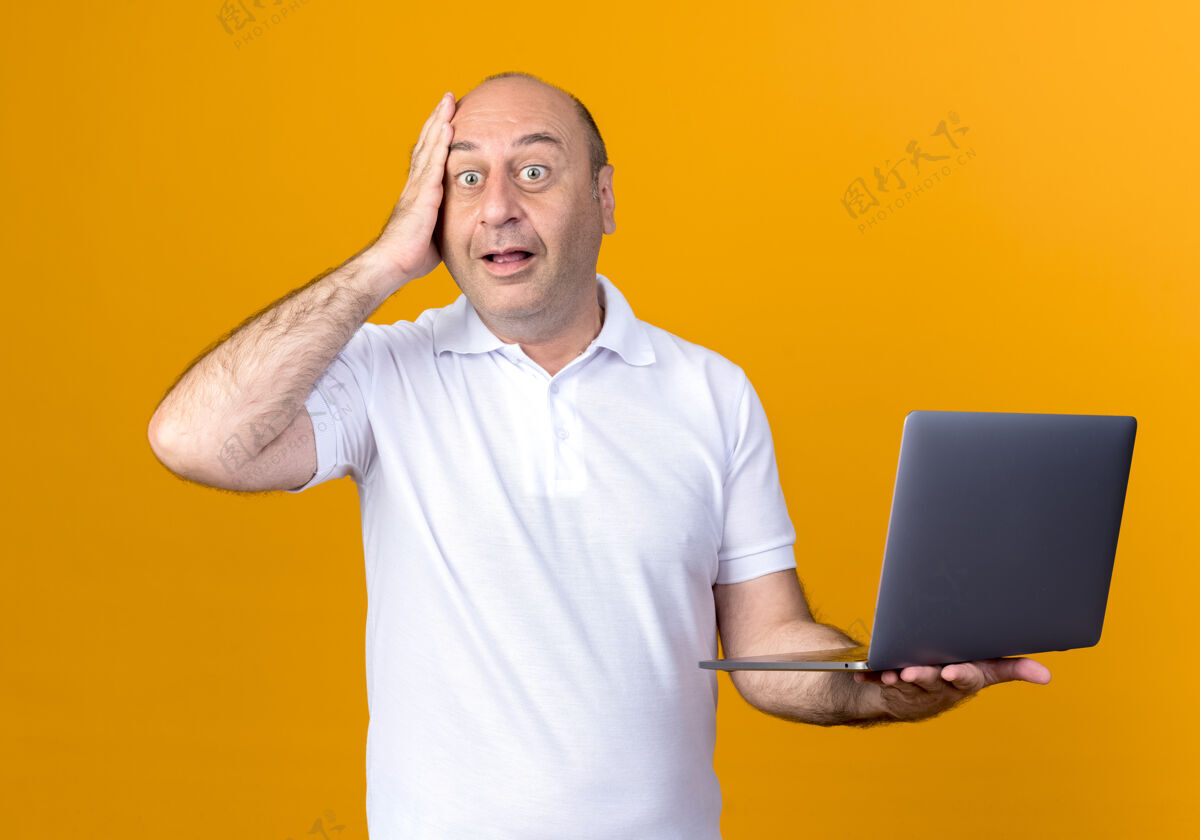 惊喜一个不经意的成熟男人拿着笔记本电脑 把手放在隔离在黄色墙上的额头上笔记本前额手