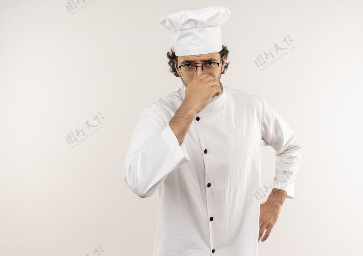 吱吱穿着厨师制服 戴着眼镜 闭着鼻子 手放在屁股上的一个神经质的年轻男厨师被隔离在白墙上烹饪男性厨师
