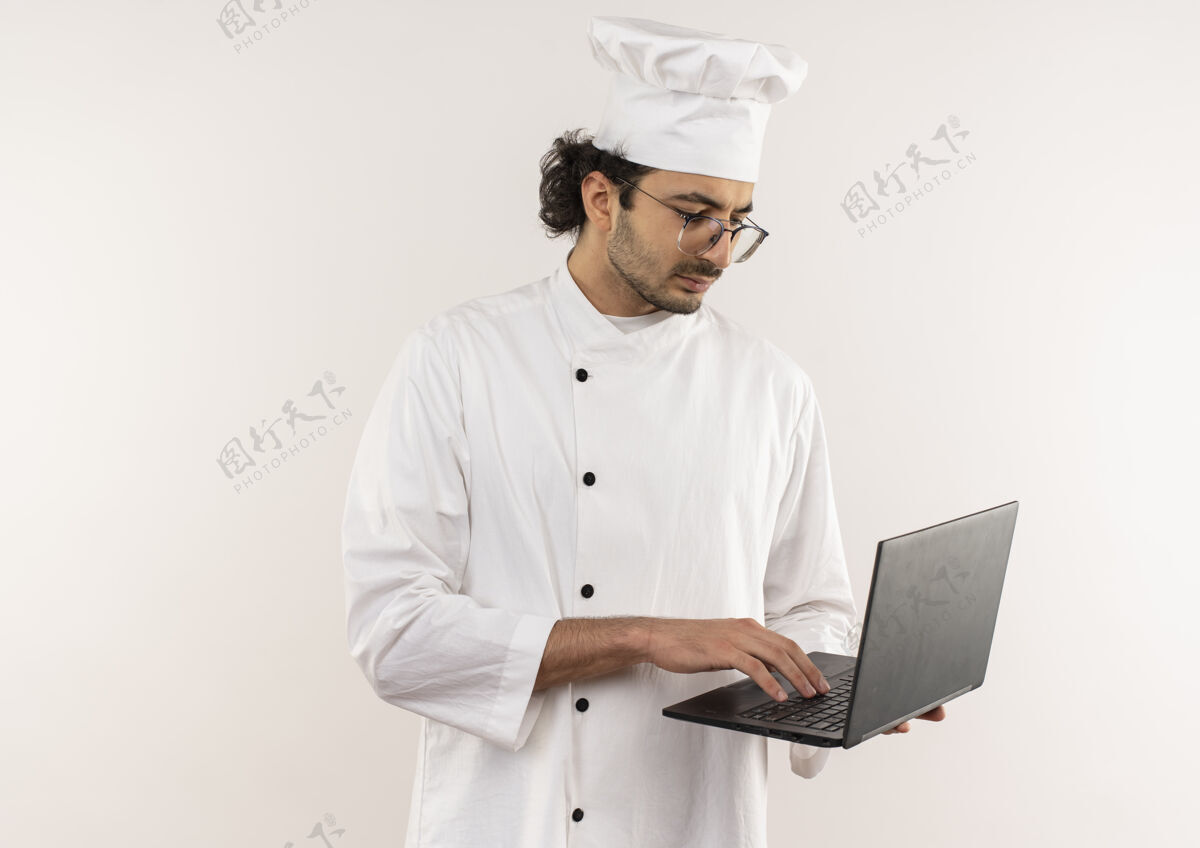 男性想着年轻的男厨师穿着厨师制服 戴着眼镜拿着和用过的笔记本电脑隔离在白墙上眼镜制服使用
