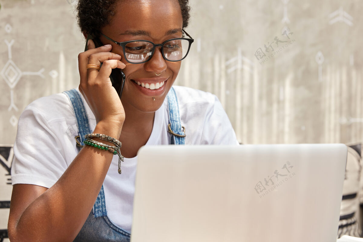 通信成功的年轻女经理在笔记本电脑上工作时通过智能手机打电话专业文件美式