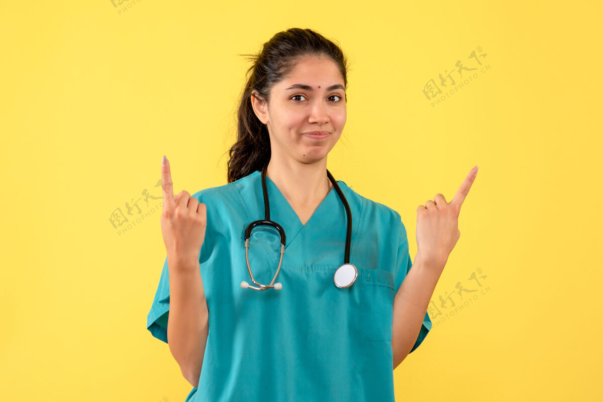 指尖年轻女医生用手指指着黄色墙壁的正视图健康护士年轻女医生